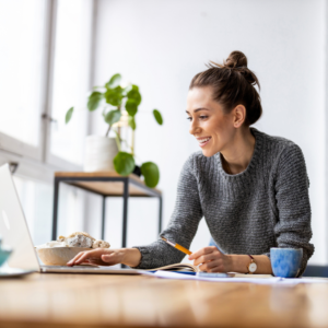 woman using laptop and writing notes in bright home office space