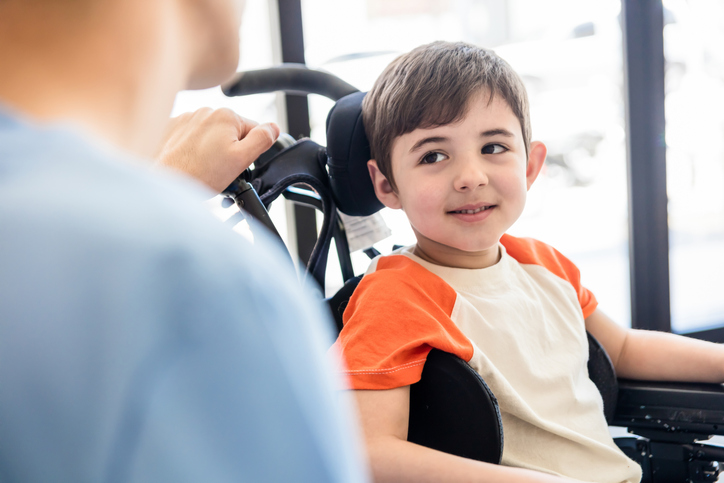 Child in wheelchair smiling at his Support Worker
