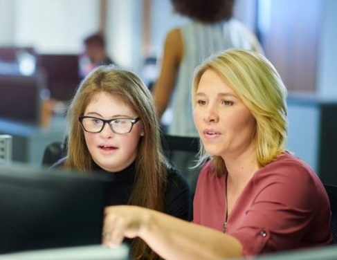young woman with down syndrome working on computer with colleague