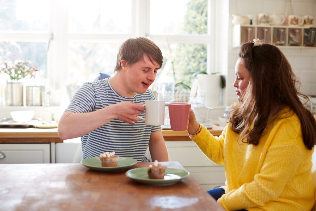 Young man living with down syndrome enjoys tea with partner in kitchen at home