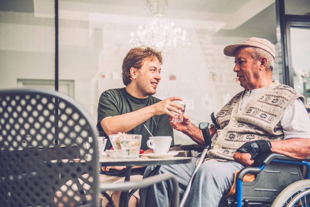 Senior Man in Wheelchair and Grandson Having Coffee, Europe