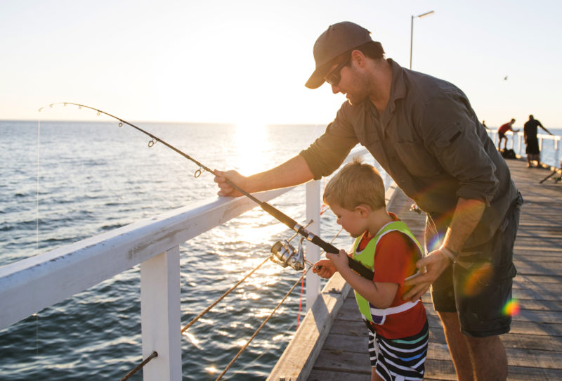 Father and young son fishing together on sea dock