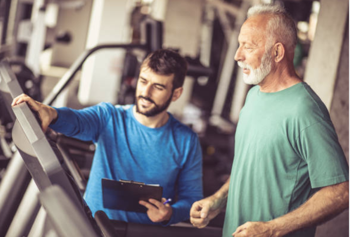 Senior man running on treadmill with fitness coach