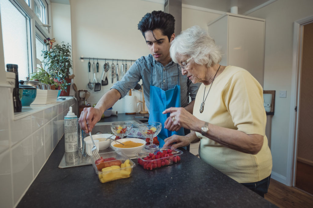 Teenage boy making fruit compote with his grandmother in the kitchen of her home.