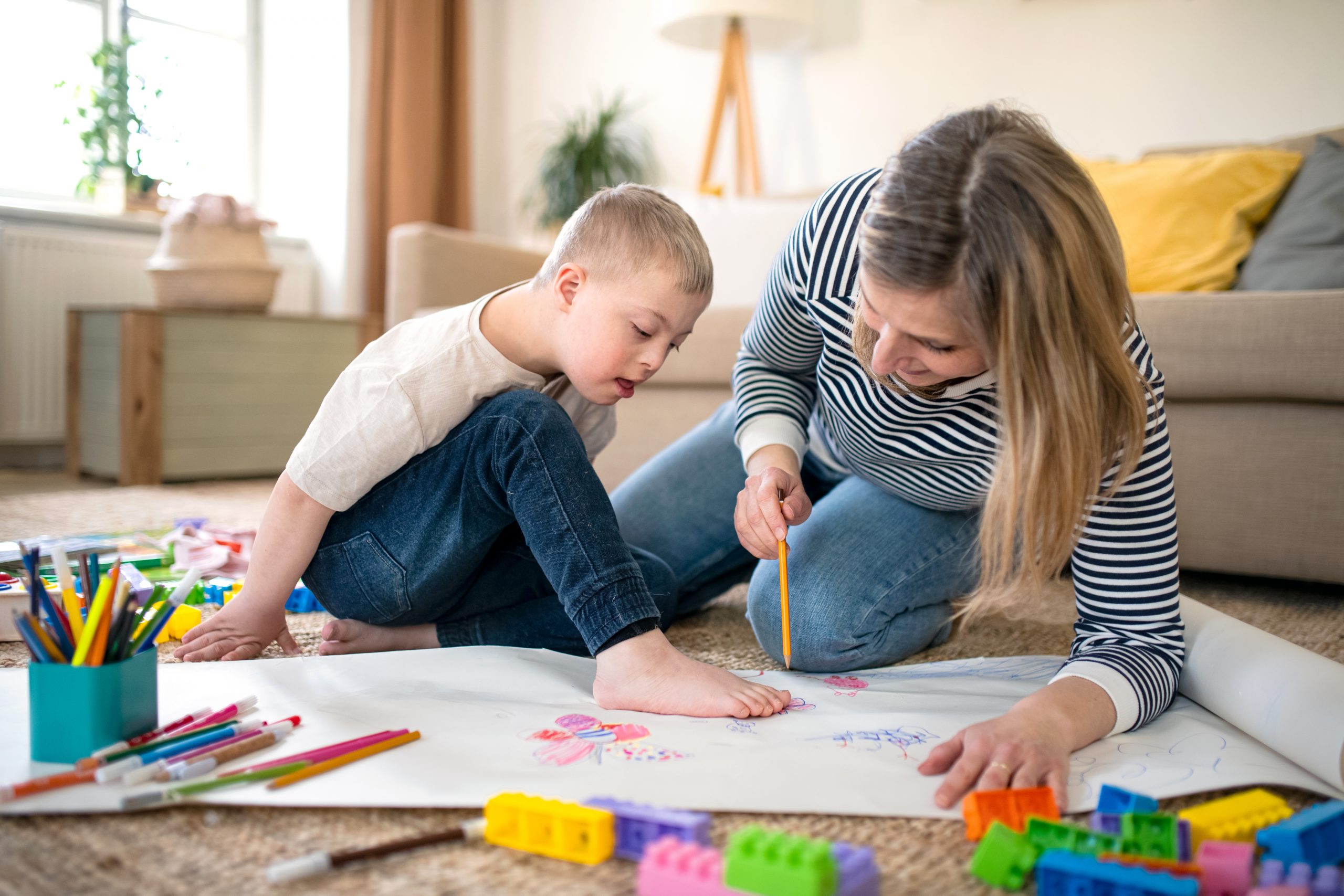 Child living with down syndrome drawing pictures with support worker in home environment