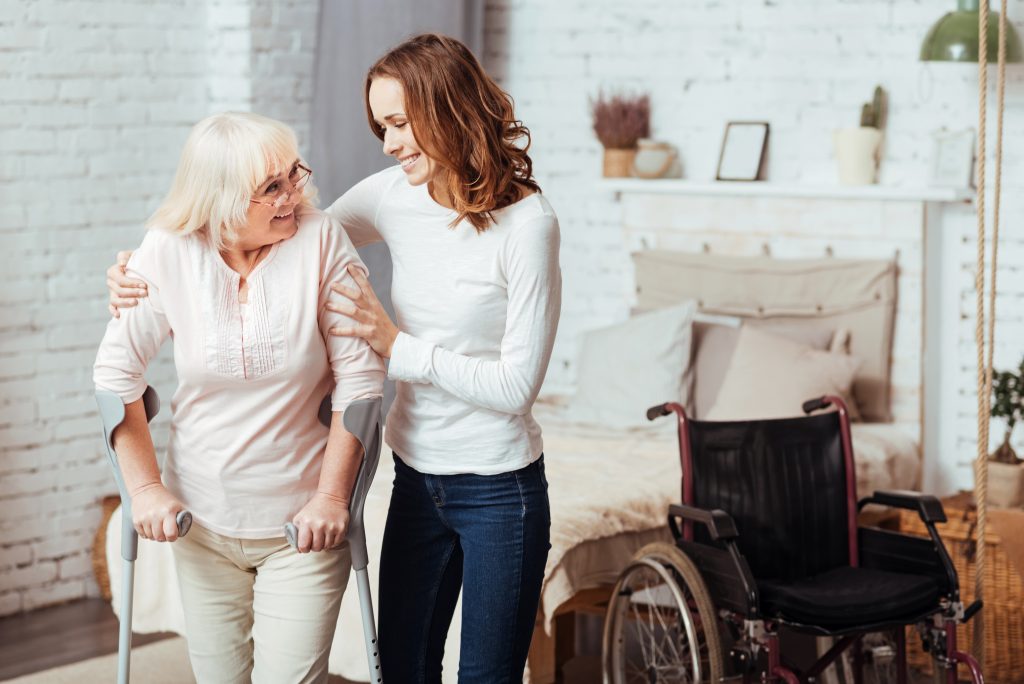 Older woman who uses crutches smiles while receiving support at home