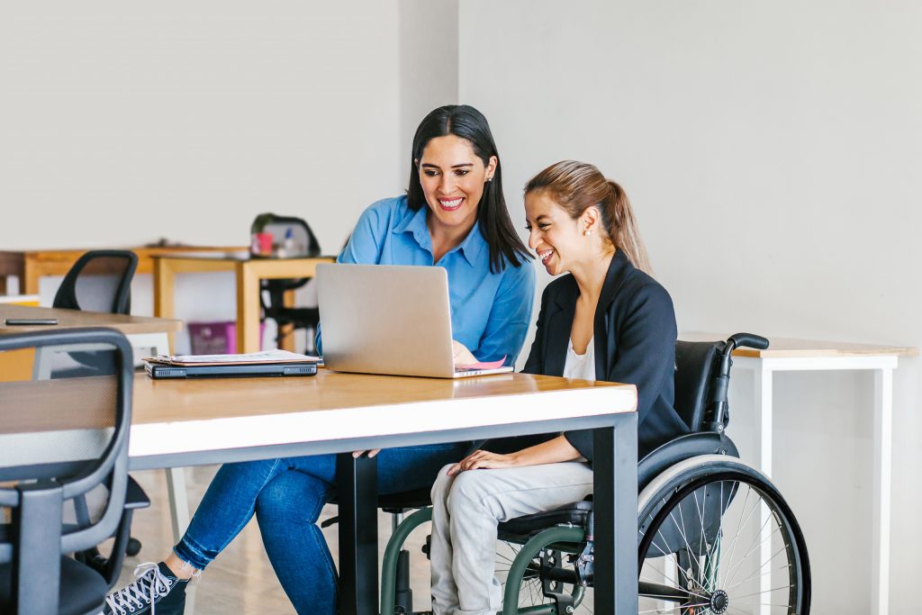 A woman using a wheelchair looks at a laptop with a support worker.