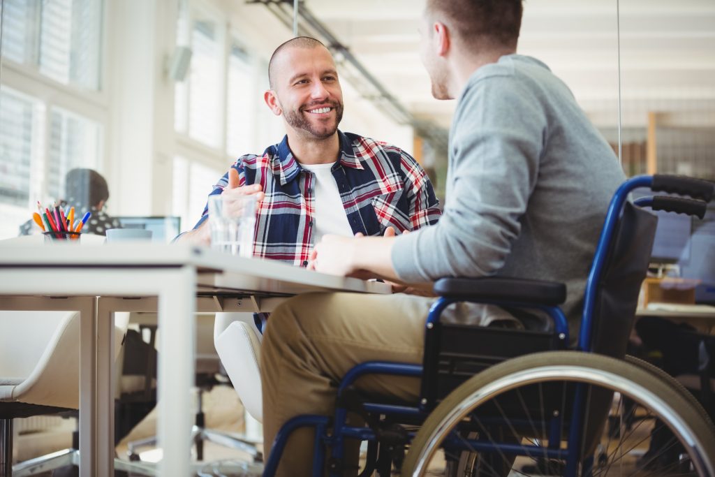 Man in wheelchair smiling at colleague in office