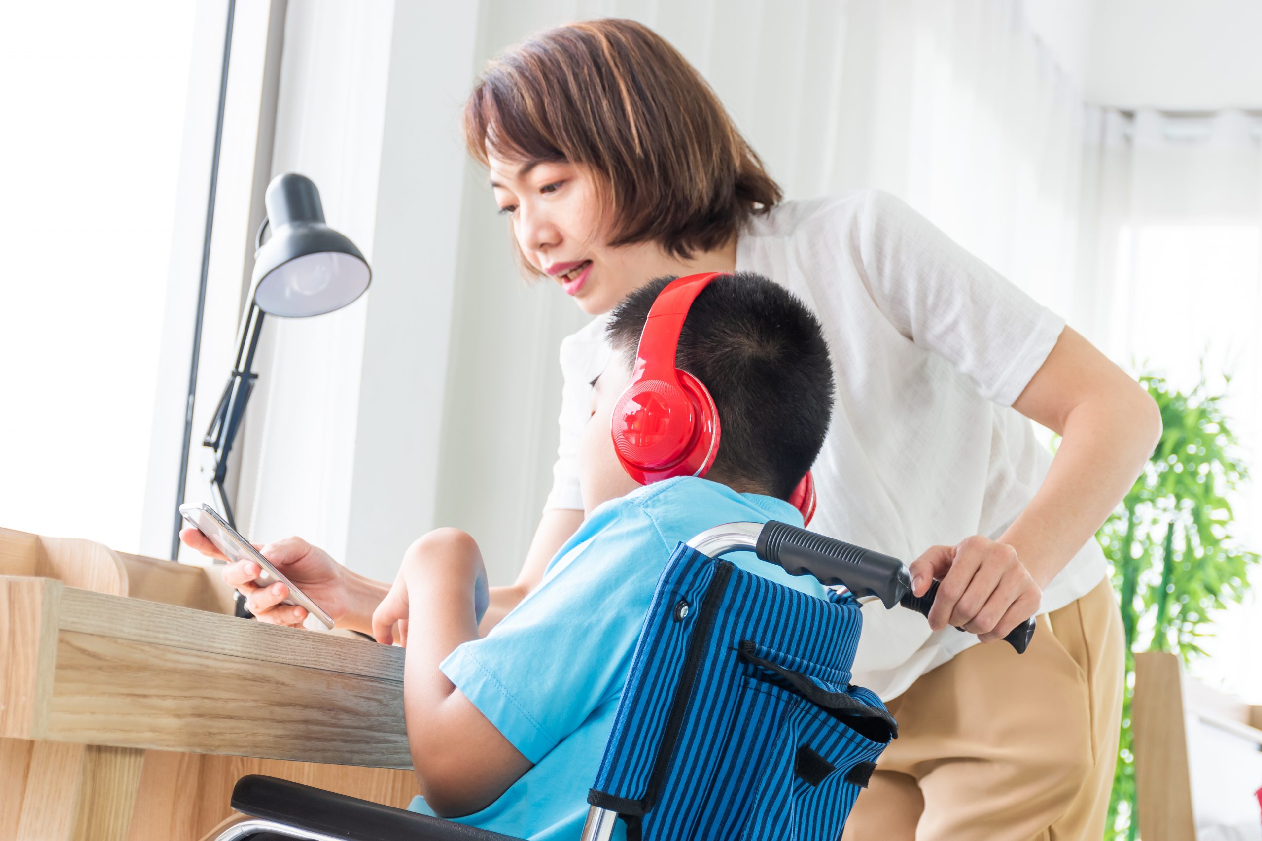 Support worker assisting child on wheelchair using smartphone