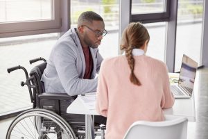 Man in wheelchair works on laptop with support worker in office environment