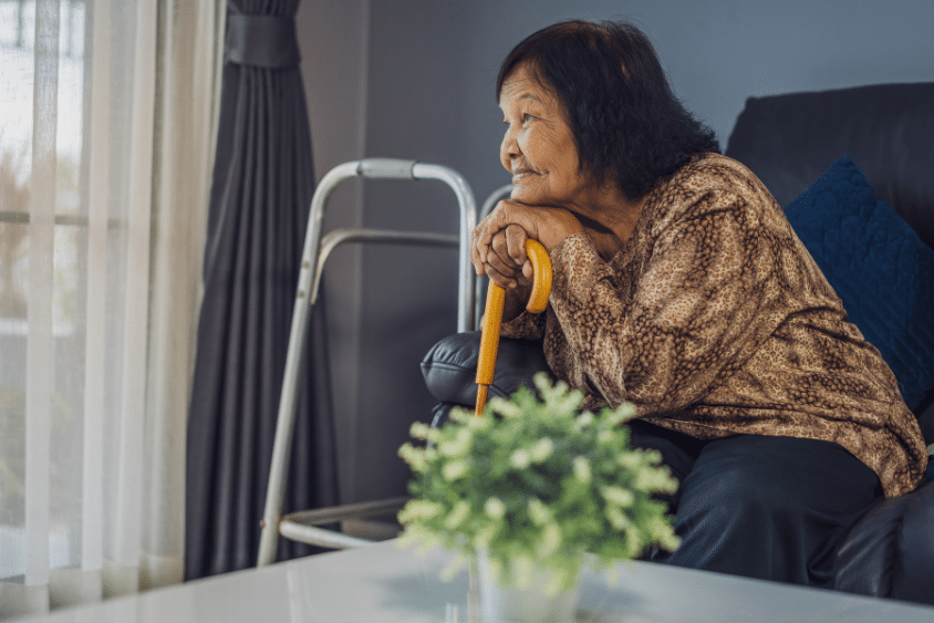 Senior woman with walking cane looking outside window at home