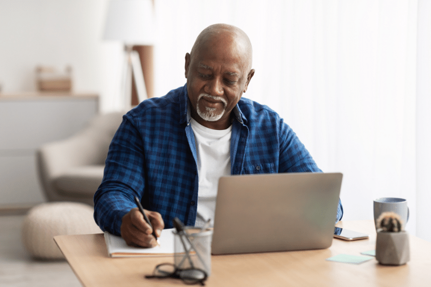 Older man taking notes with laptop at home