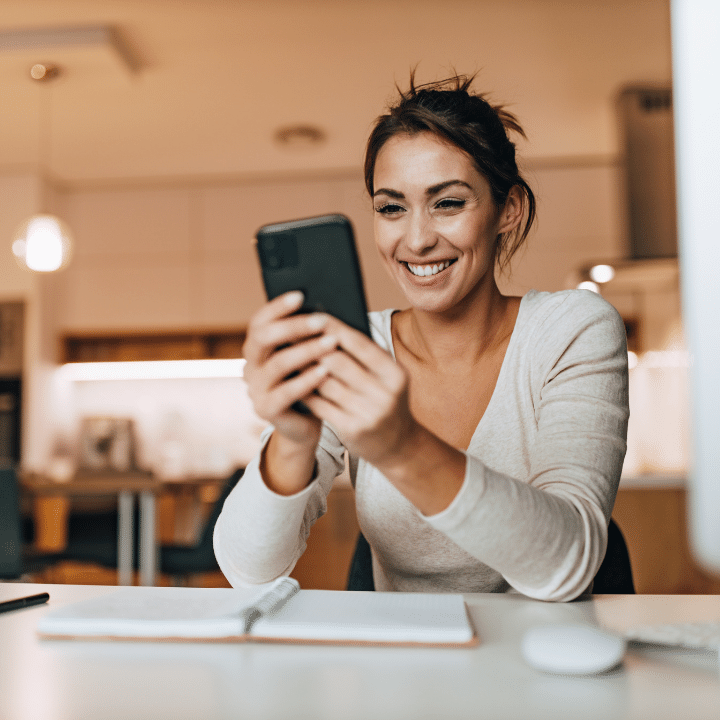 woman smiling while using phone at home office