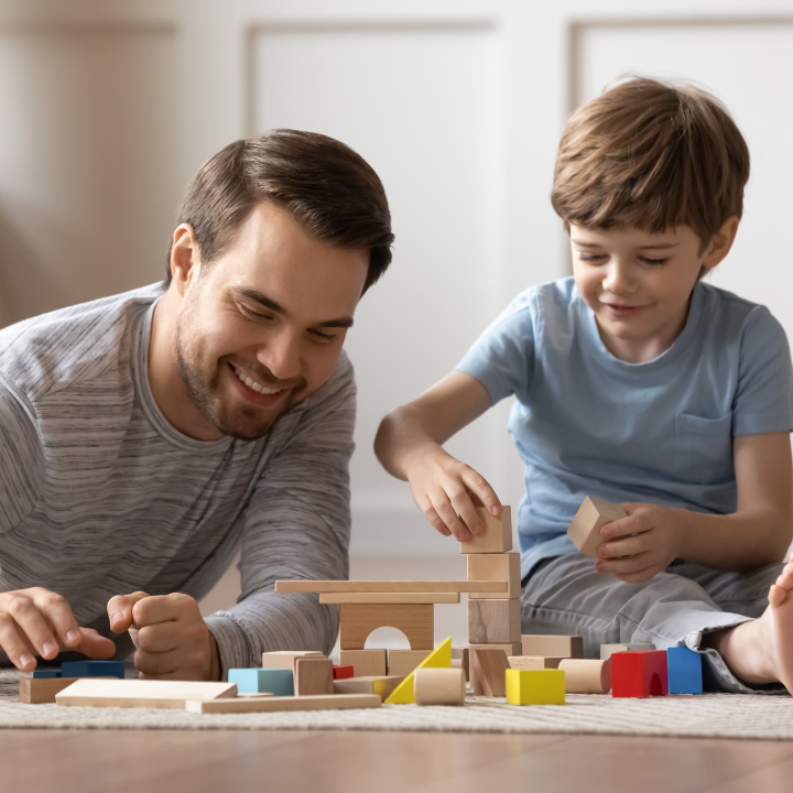 father and young child playing with colourful blocks on home living room floor