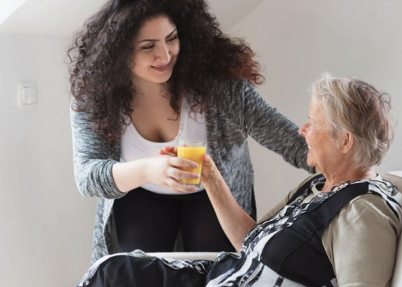 A support worker handing her aged care client a drink.