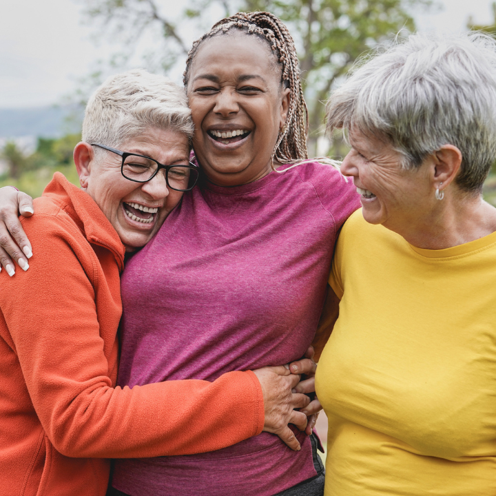 Three diverse senior women embrace in park, smiling