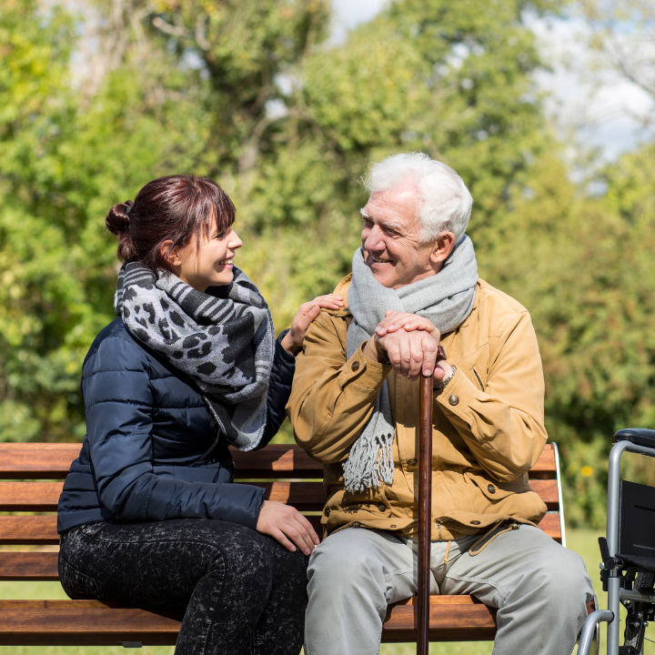 An older man and his support worker sitting on a park bench together.
