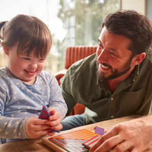 A young child with Down syndrome and a support worker playing with blocks together.