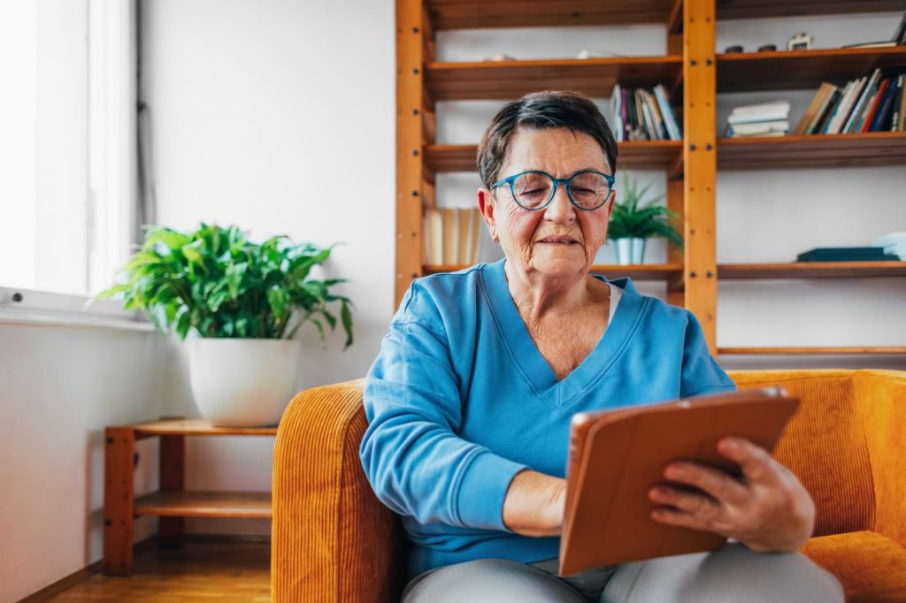 An older woman sitting on a couch using a tablet.