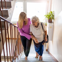 Support worker helping her elderly client walk up the stairs