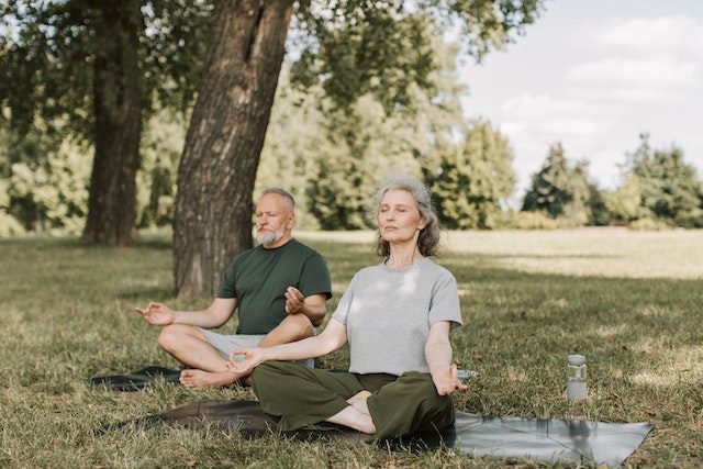 elderly couple sitting in a park and meditating