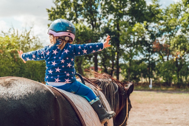 toddler riding a horse excitedly with her arms out