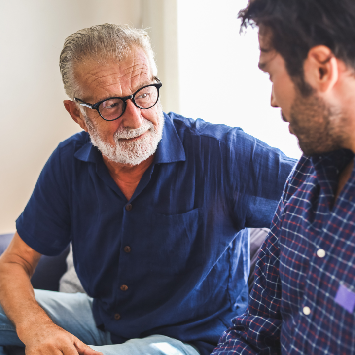 senior man in glasses having conversation with young support worker in living room