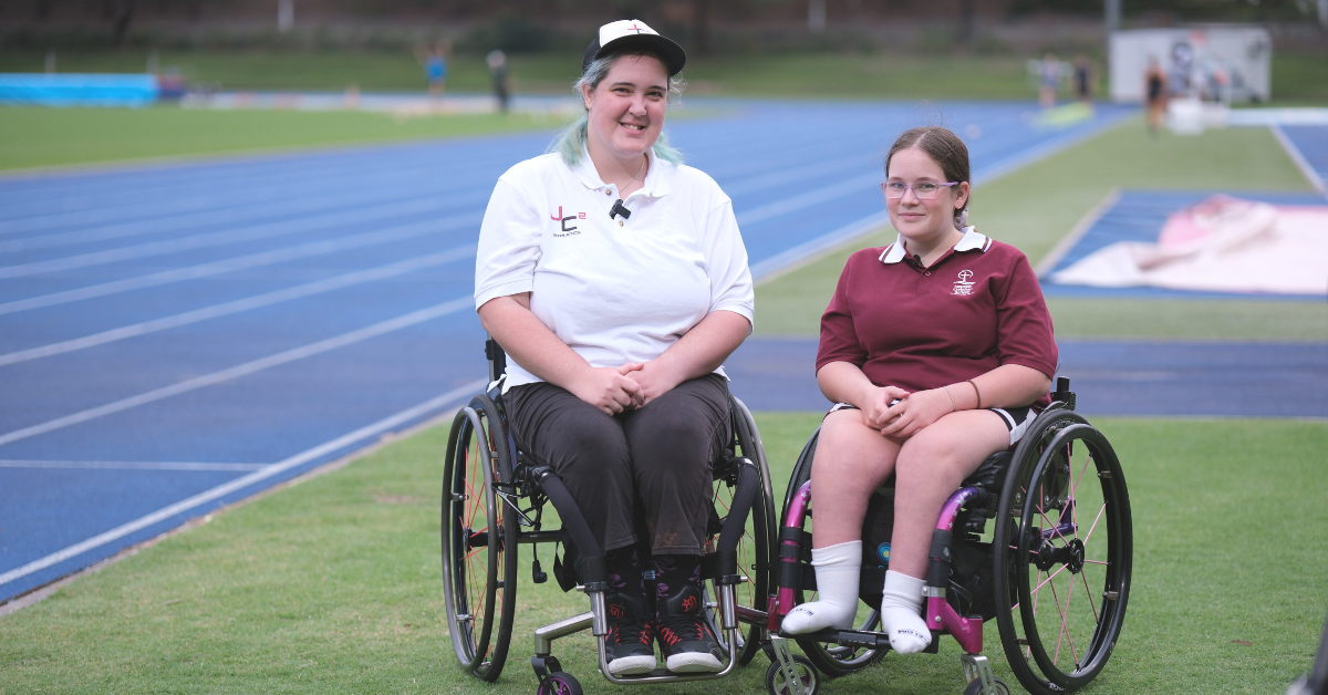 Para-athlete Julie Charlton on an athletics field beside another young female wheelchair user.