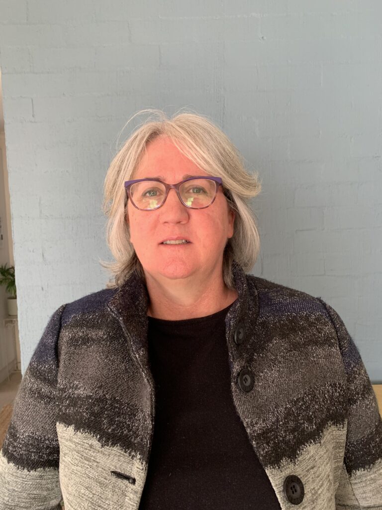 Donna is looking at the camera wearing glasses and a coat.