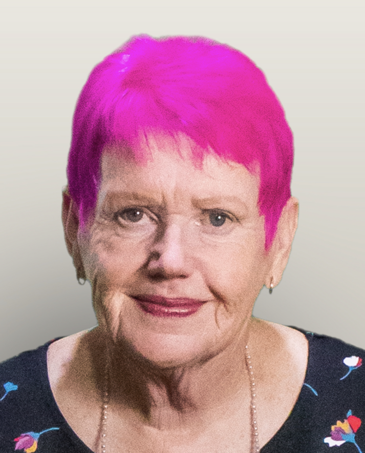 Portrait of Gwenda Darling. She has pink hair and red lipstick and is smiling at the camera.
