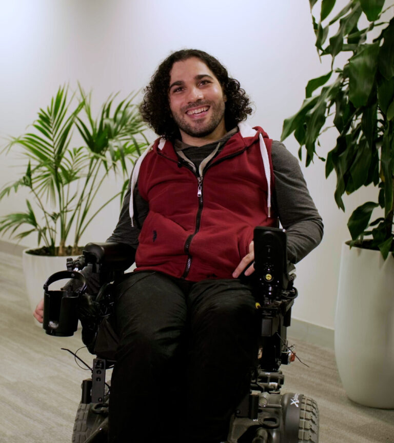 Moustafa, in electric wheelchair, smiles at Mable office