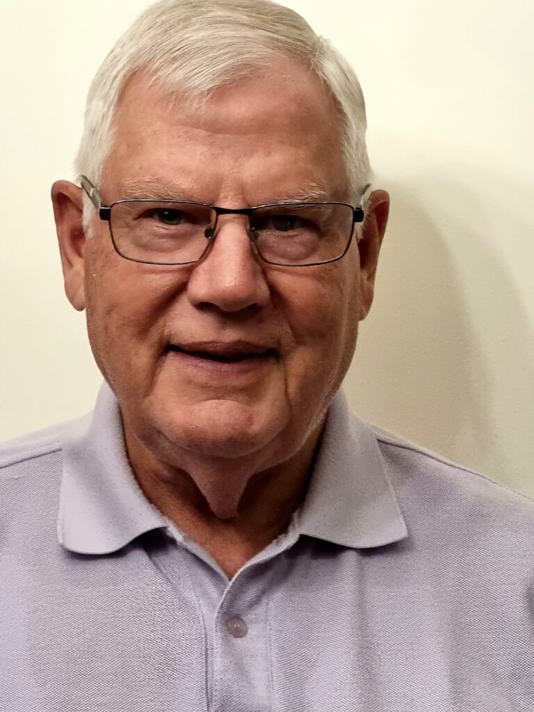 Will Charlton smiling at camera. He is wearing glasses and a violet polo top.