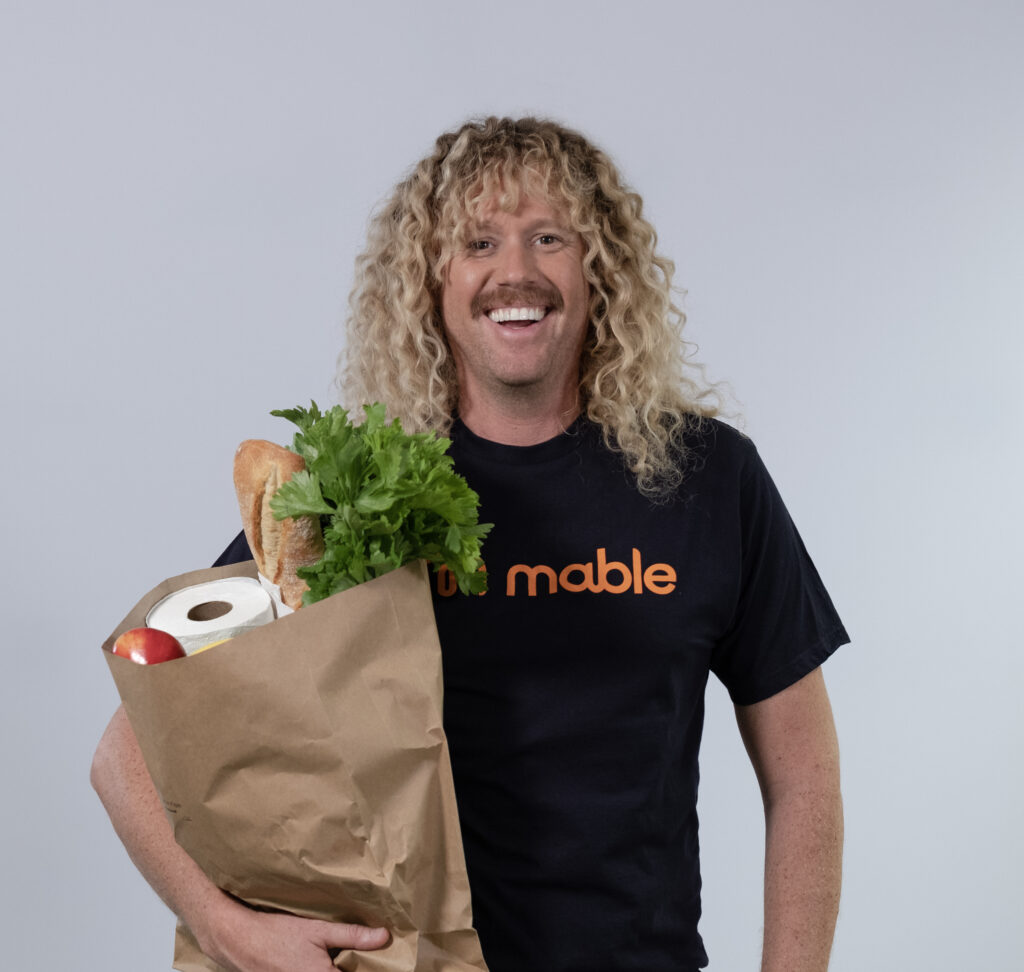 Tim Dormer. He has long curly hair and a moustache, and is holding a bag of groceries.