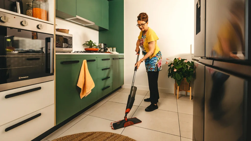 Support worker mops the kitchen floor in their client’s home.