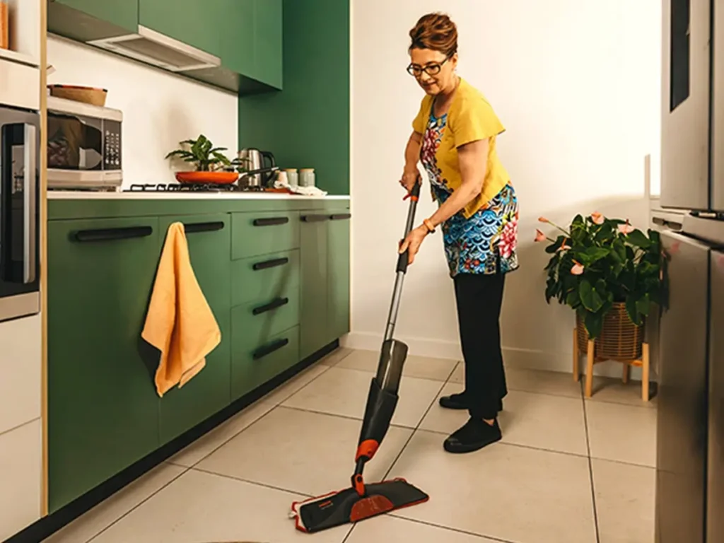 Support worker mops the kitchen floor in their client’s home.
