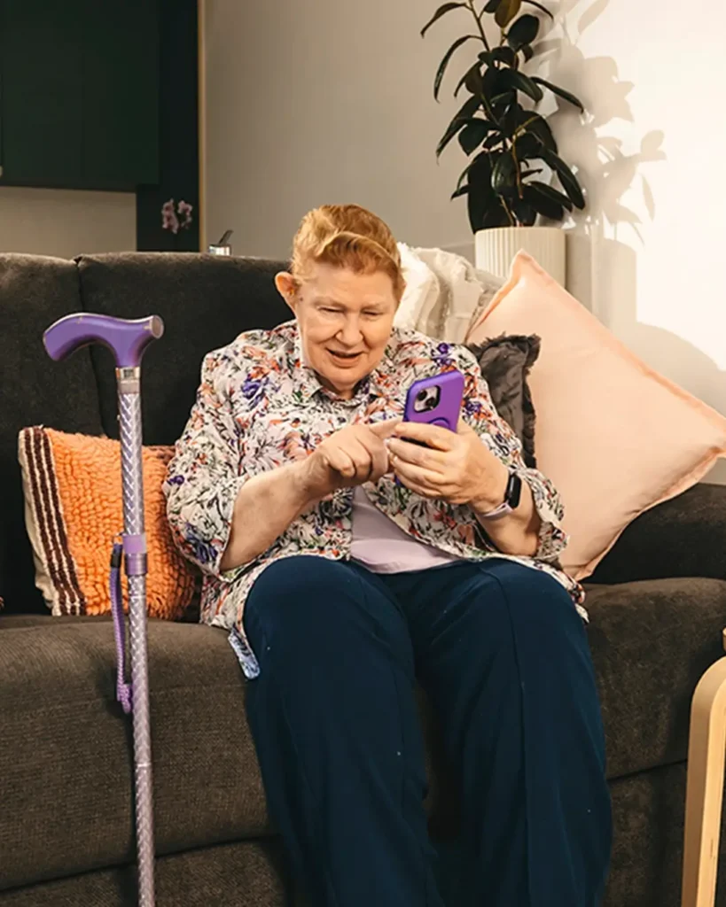 Older person with a walking stick at home using mobile phone to find support on Mable.