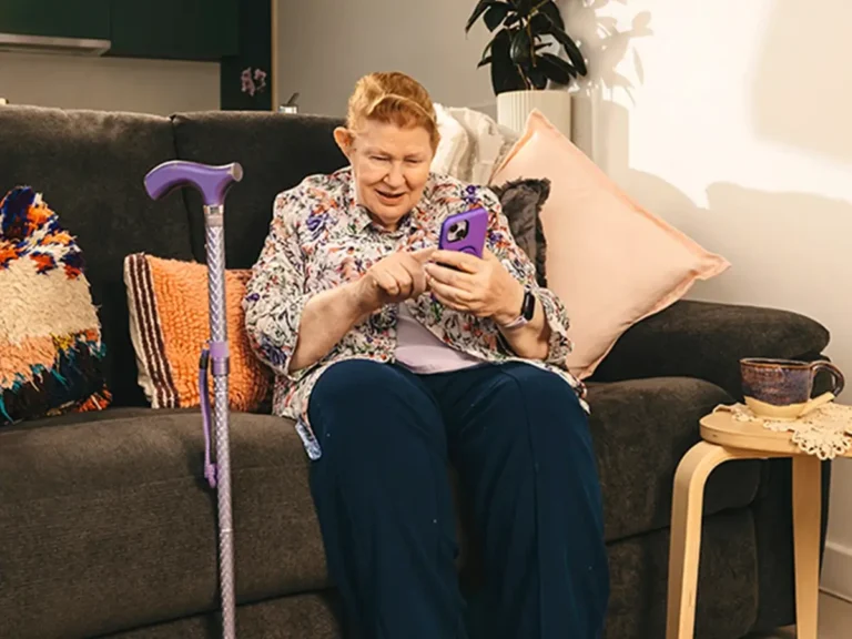 Older person with a walking stick at home using mobile phone to find support on Mable.