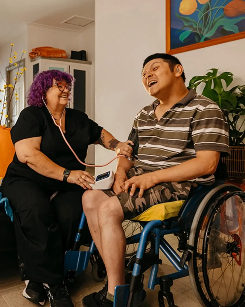 Registered Nurse takes blood pressure reading of client with cerebral palsy in wheelchair.