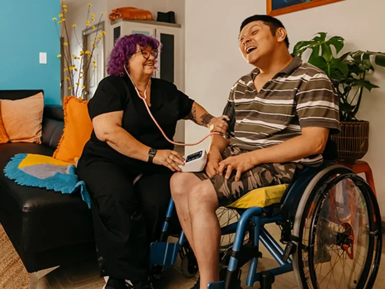 Registered Nurse takes blood pressure reading of client with cerebral palsy in wheelchair.