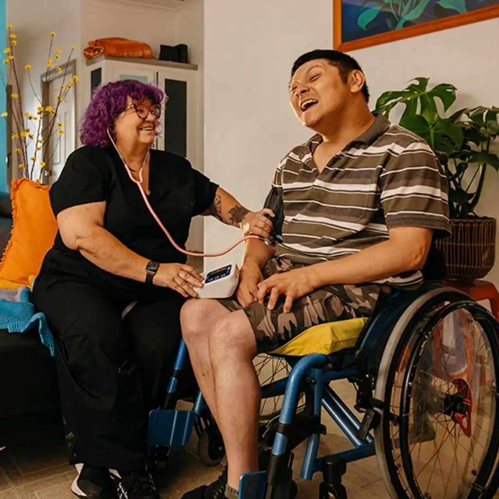 Registered Nurse takes blood pressure reading of client with cerebral palsy in wheelchair.