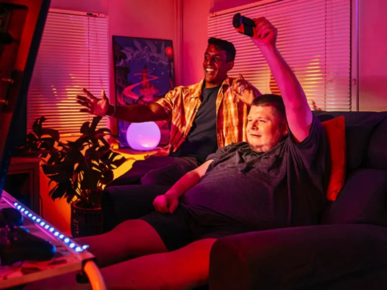 Support worker and person with disability celebrate video game win in a pink neon-lit gamer room.