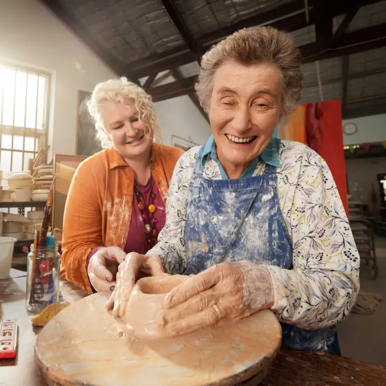 Two people are turning clay while smiling in a studio.