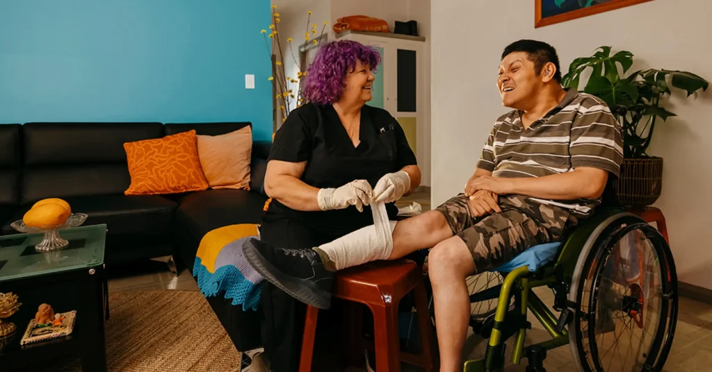 Registered Nurse bandages leg of client with cerebral palsy in wheelchair.