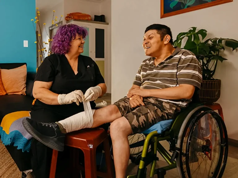 Registered Nurse bandages leg of client with cerebral palsy in wheelchair.