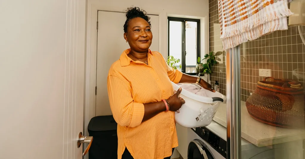 Support worker carries a washing basket on hip through the laundry at their client’s home.