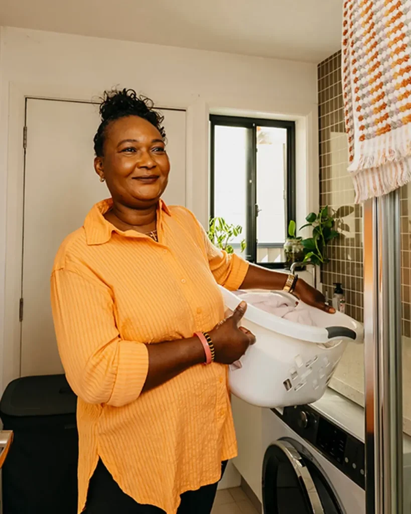 Support worker carries a washing basket on hip through the laundry at their client’s home.