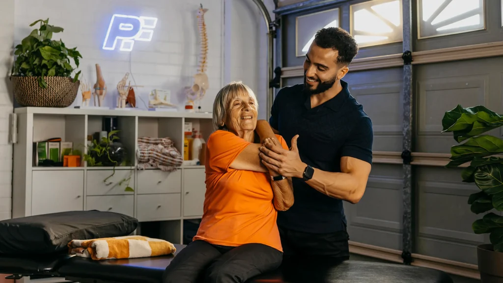 Physiotherapist supports older client’s arm and back during arm stretch over the shoulder.
