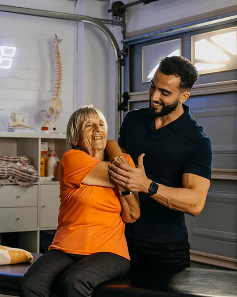Physiotherapist supports older client’s arm and back during arm stretch over the shoulder.