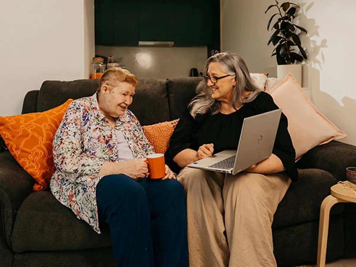 Support coordinator sits with an older client and their laptop to search support workers on Mable.