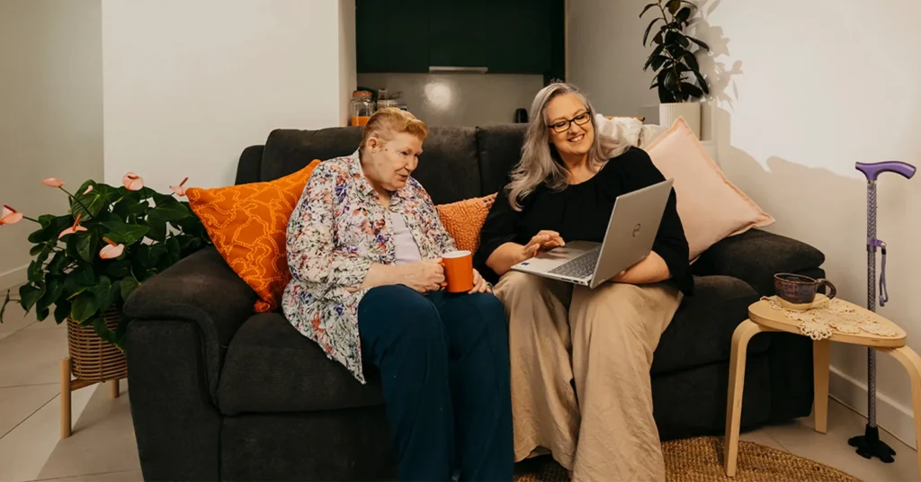 Support coordinator sits with an older client and their laptop to search support workers on Mable.